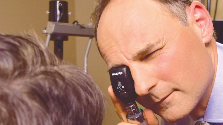 David P. Montesanti, a board-certified surgeon with Eye Care & Vision Associates, uses an ophthalmoscope to examine a patient’s eyes.