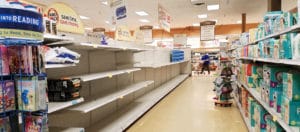 A lone shopper gazes down an aisle of mostly empty shelves at a local Wegmans.